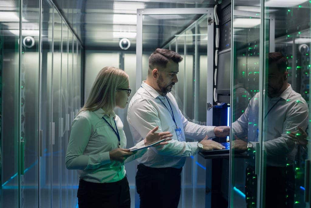 man and woman using tablet and laptop while diagnosing server hardware in modern data center in Utah