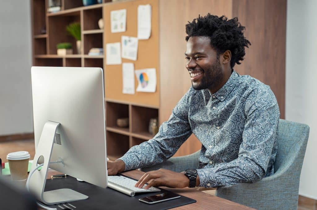 African American man working on mac desktop while smiling