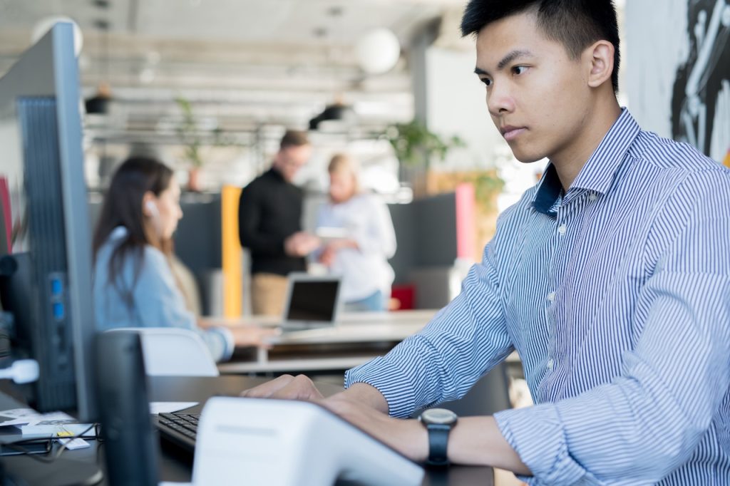 employee typing on computer in office near coworkers